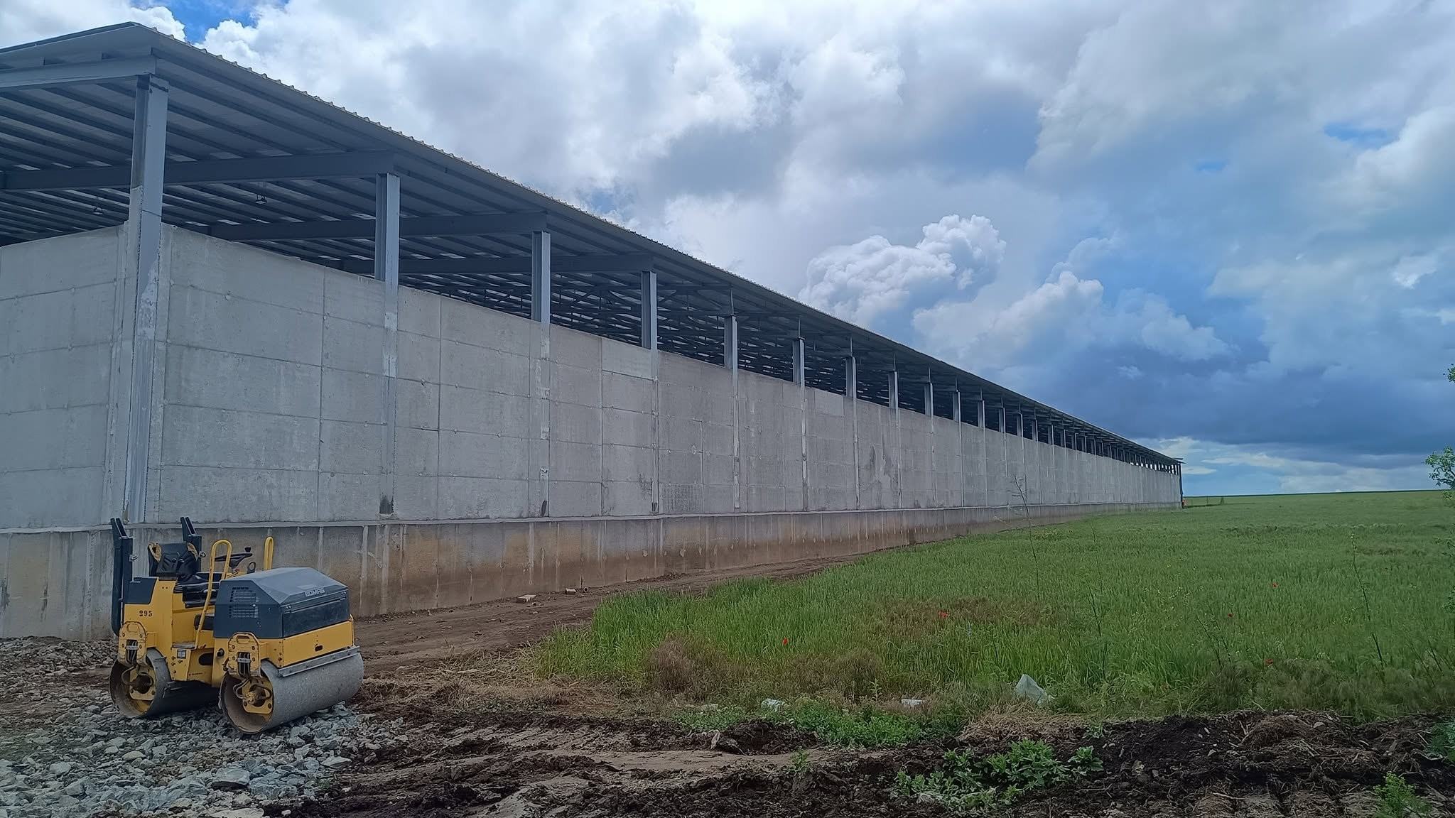 Hală lungă cu pereți din beton prefabricat, lângă un câmp verde